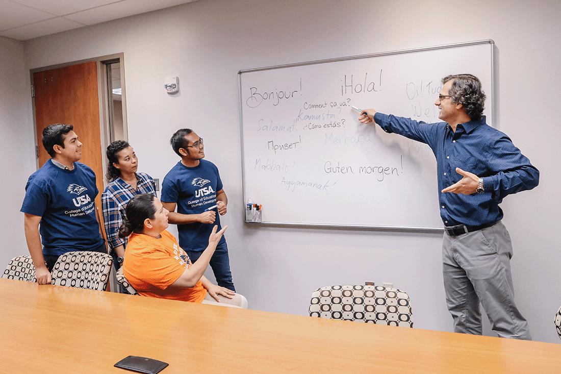 Professor pointing at whiteboard showing students dual language information