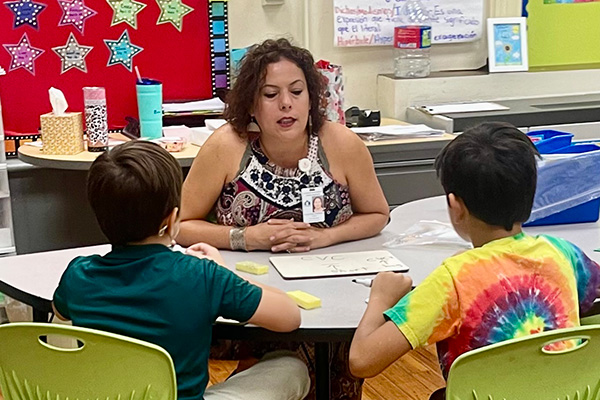 An SAISD teacher is working with two students at a small group table.
