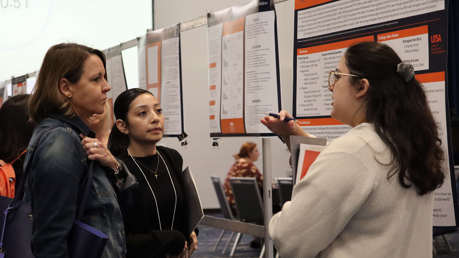 A student discusses their research project with a professor and fellow student.