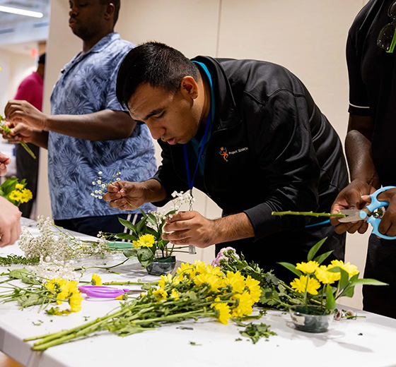 Employ 210 participant Eric Guerrero practices making floral arrangements during a job experience event for neurodiverse individuals at the ZerNona Black Multigenerational Community Center 